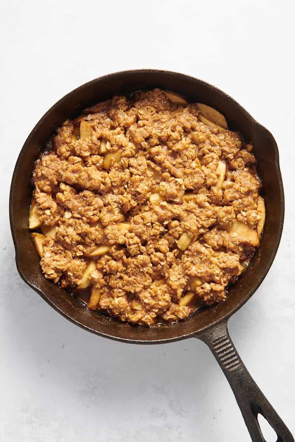 sliced apples dressed in cinnamon and nutmeg poured into a cast iron skillet topped with a crumble mixture