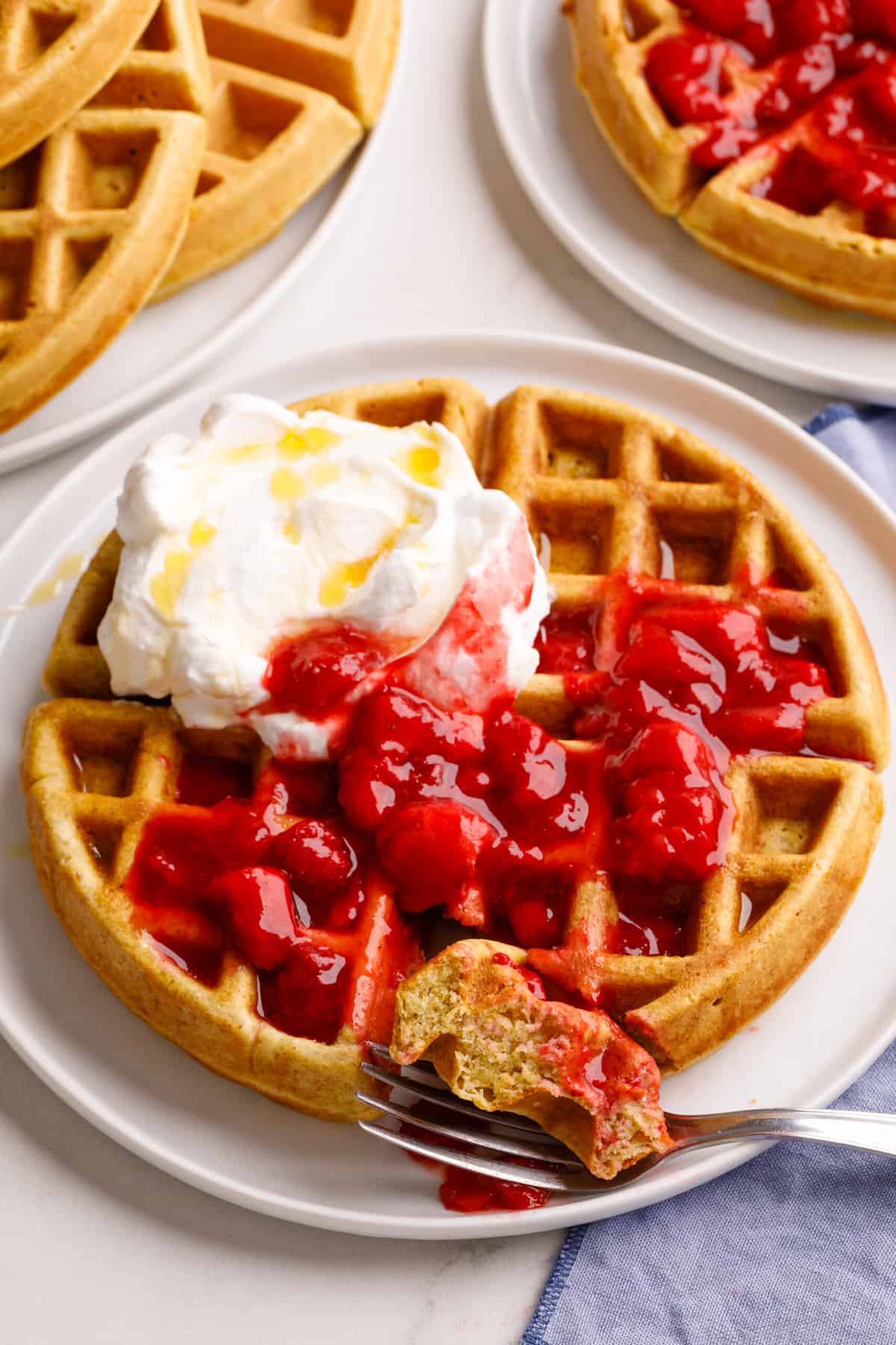 a sourdough waffle topped with strawberry compote and whipped cream sitting on a white round plate