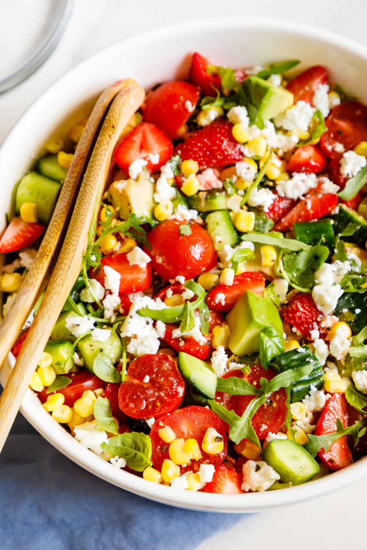 close up image of a large bowl of summer salad with wooden salad mixing utensils