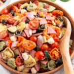 A bowl of tortellini pasta salad with a wooden spoon on the side.