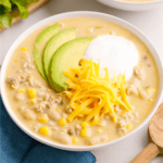 A bowl of white bean chicken chili topped with cheese, yogurt, and avocado slices.