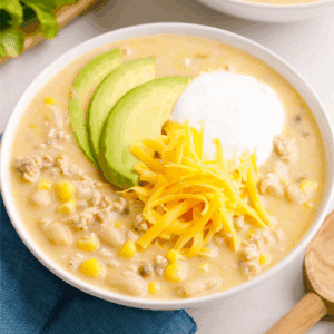 A bowl of white bean chicken chili topped with cheese, yogurt, and avocado slices.