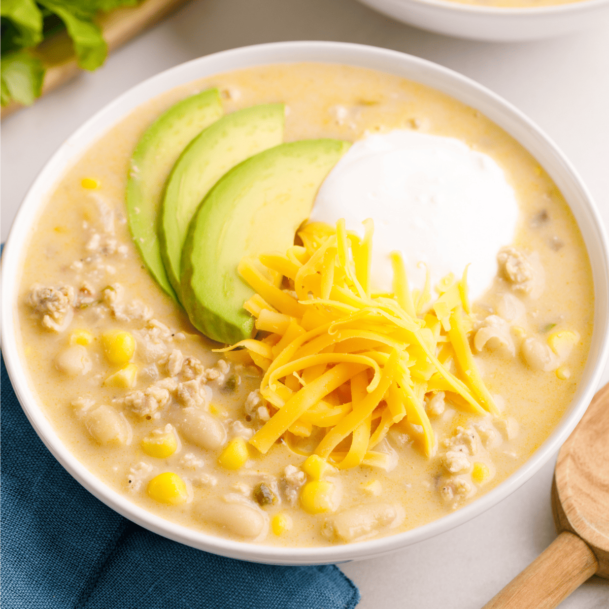 A bowl of white bean chicken chili topped with cheese, yogurt, and avocado slices.