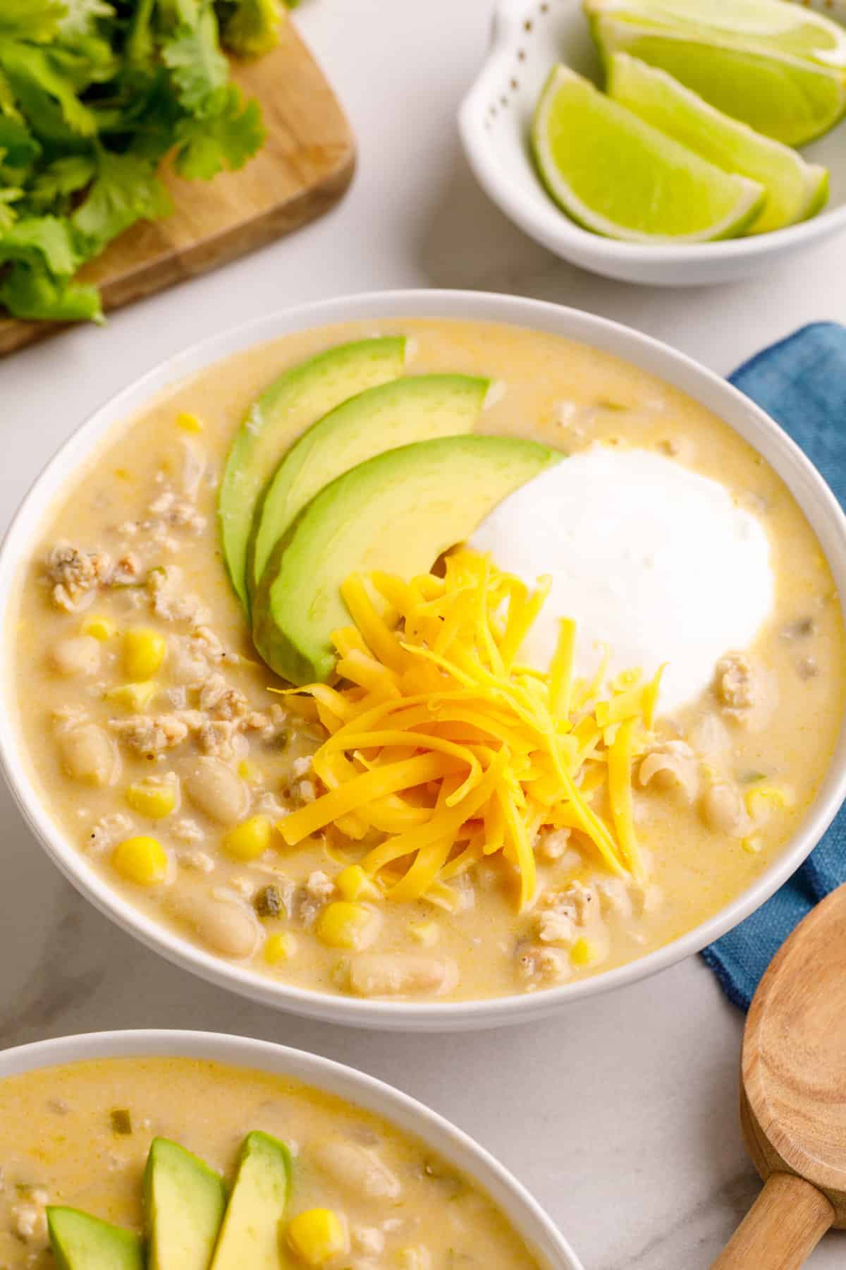 close up image of a bowl of white bean chicken chili topped with sliced avocados, sour cream and shredded cheddar cheese