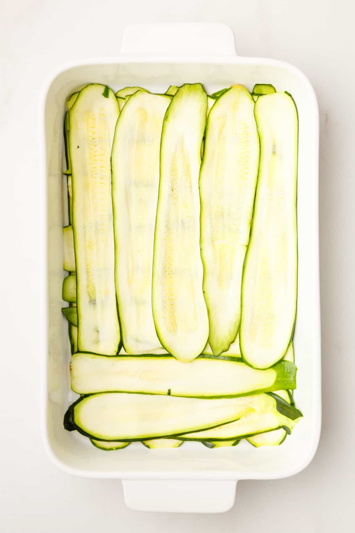 thinly sliced zucchini layered at the bottom of a 9x13 casserole dish.