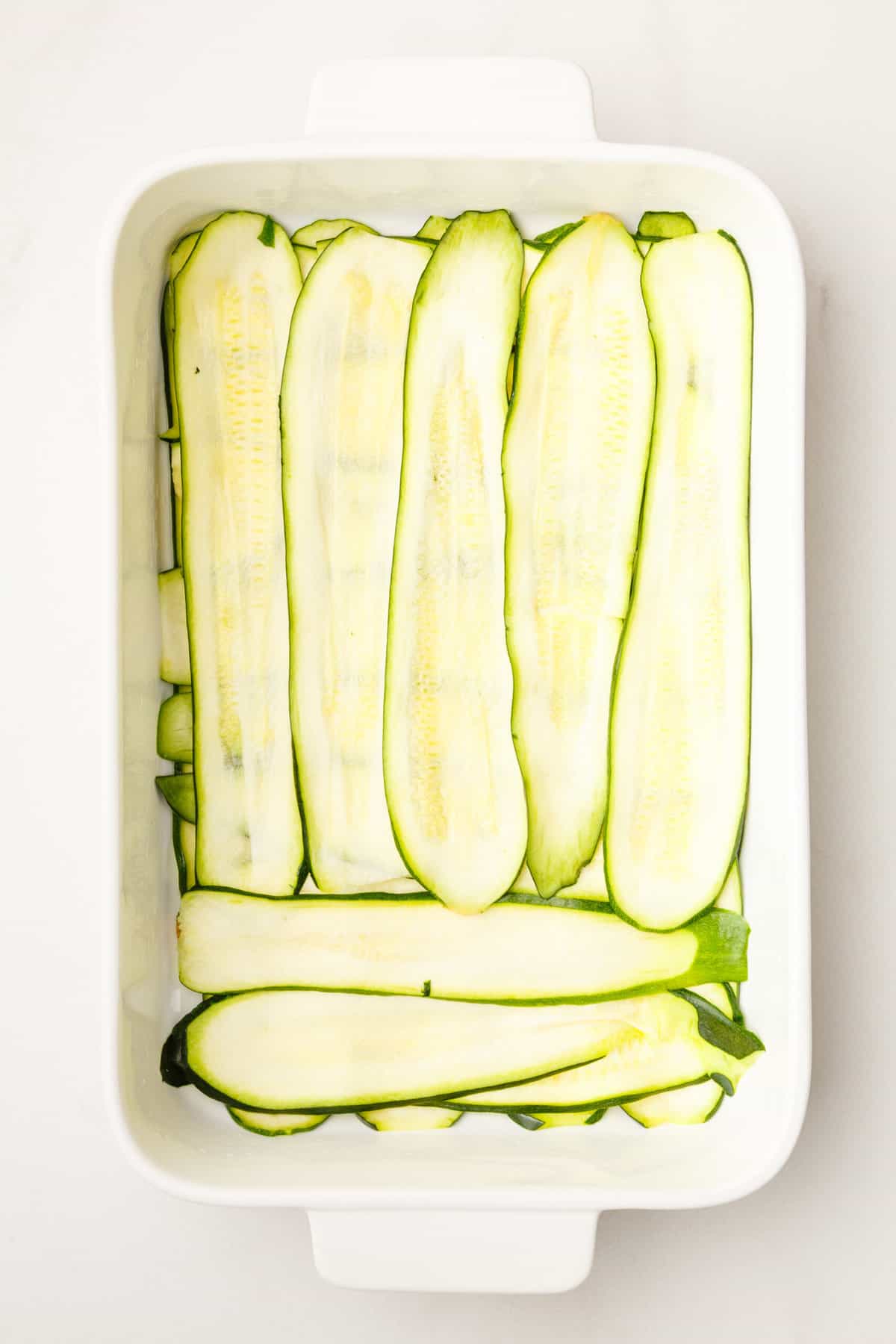 thinly sliced zucchini layered at the bottom of a 9x13 casserole dish