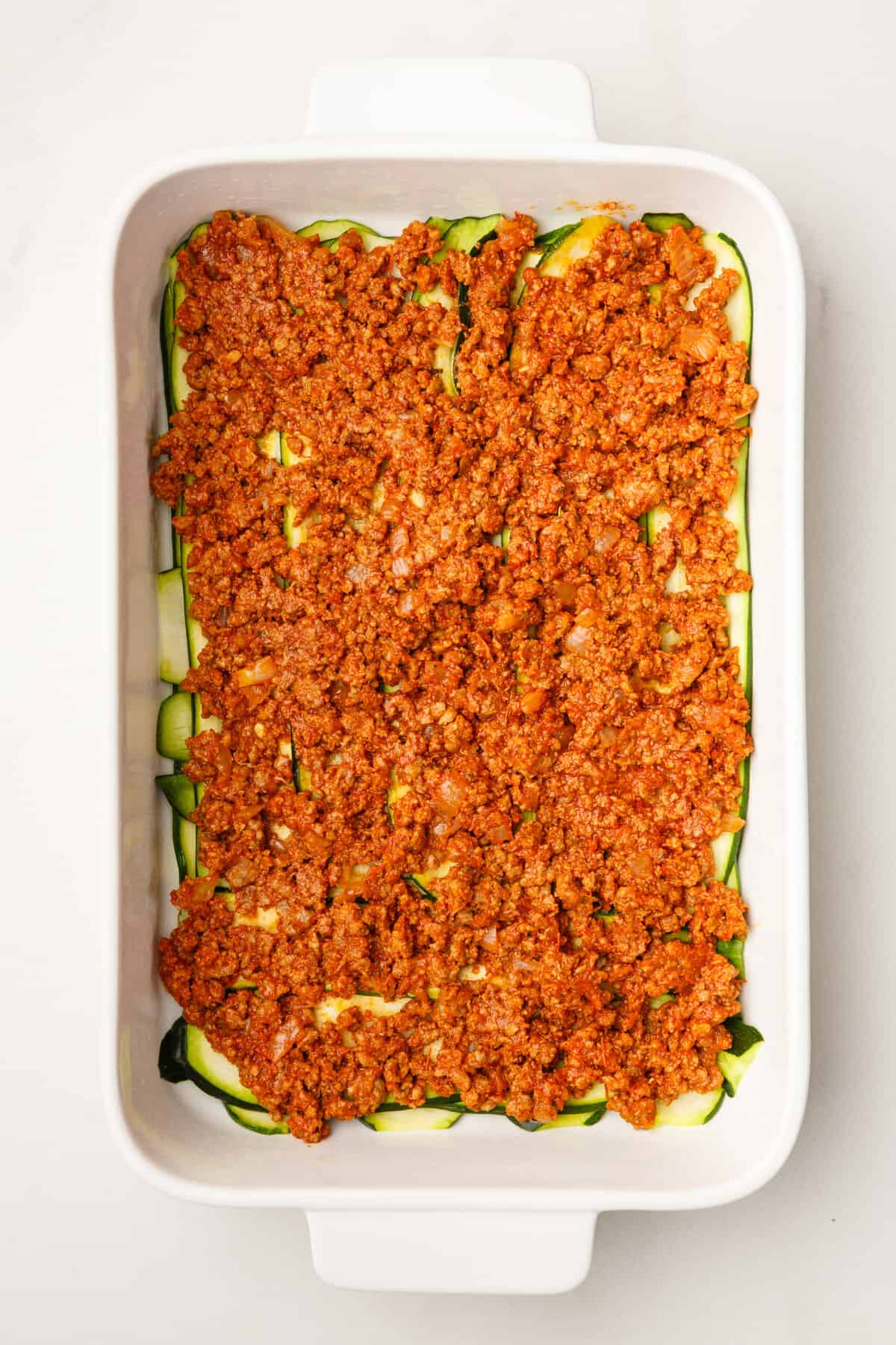 thinly sliced zucchini layered at the bottom of a 9x13 casserole dish topped with hearty tomato based ground beef