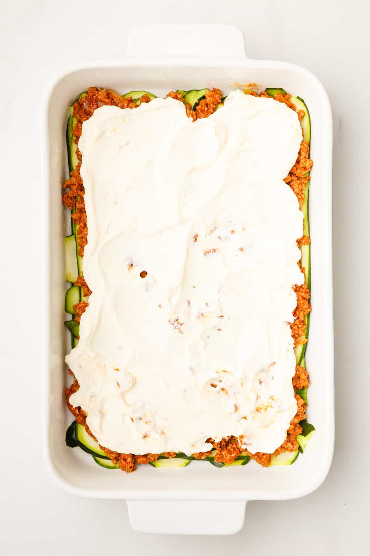 thinly sliced zucchini layered at the bottom of a 9x13 casserole dish topped with hearty tomato based ground beef and ricotta cheese