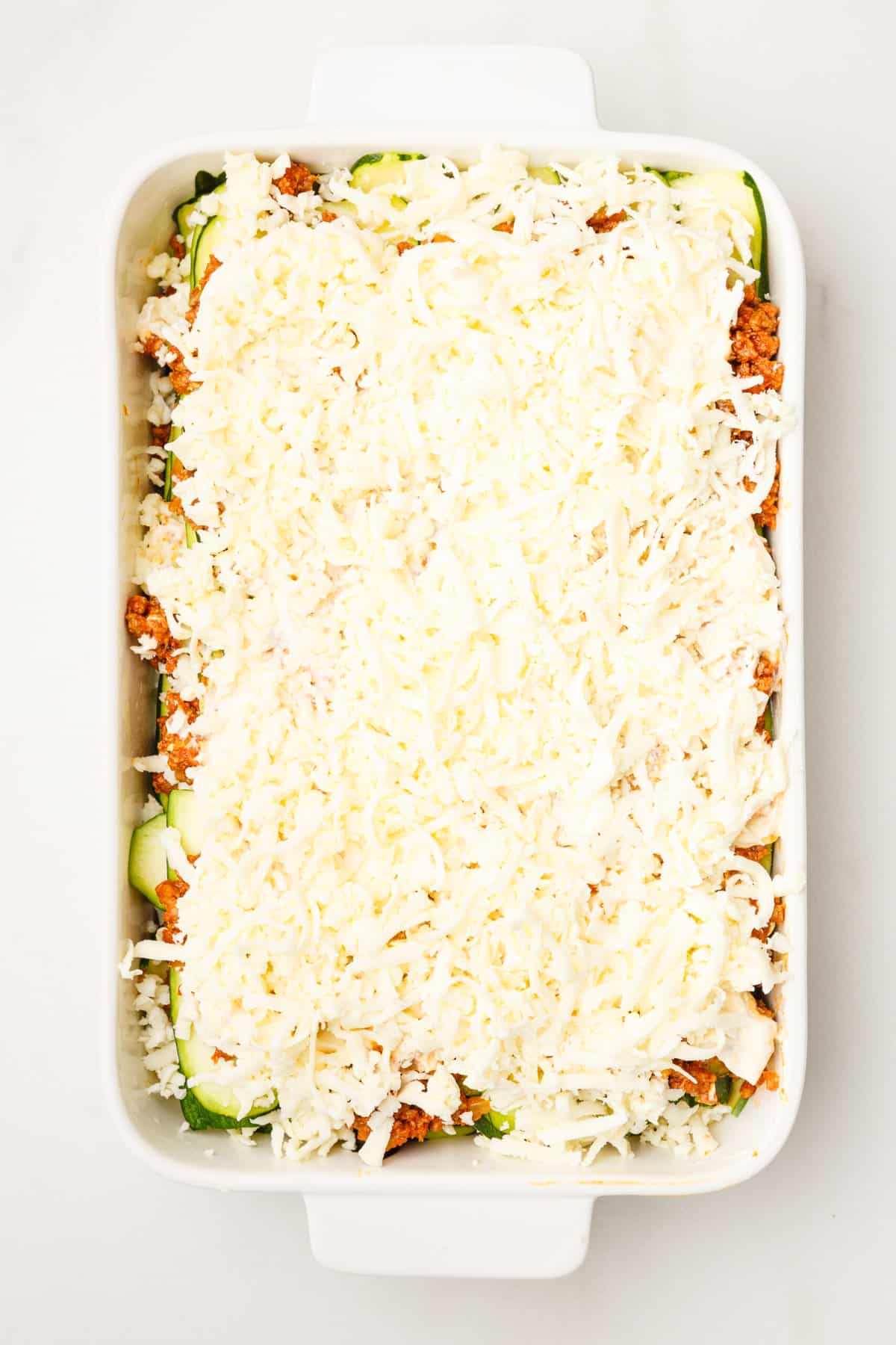 thinly sliced zucchini layered at the bottom of a 9x13 casserole dish topped with hearty tomato based ground beef and ricotta cheese and shredded mozzarella cheese