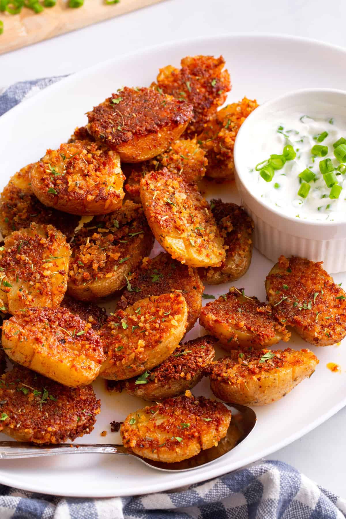 close up image of crispy parmesan potatoes served on a large white oval plate with a side of green onion dipping sauce