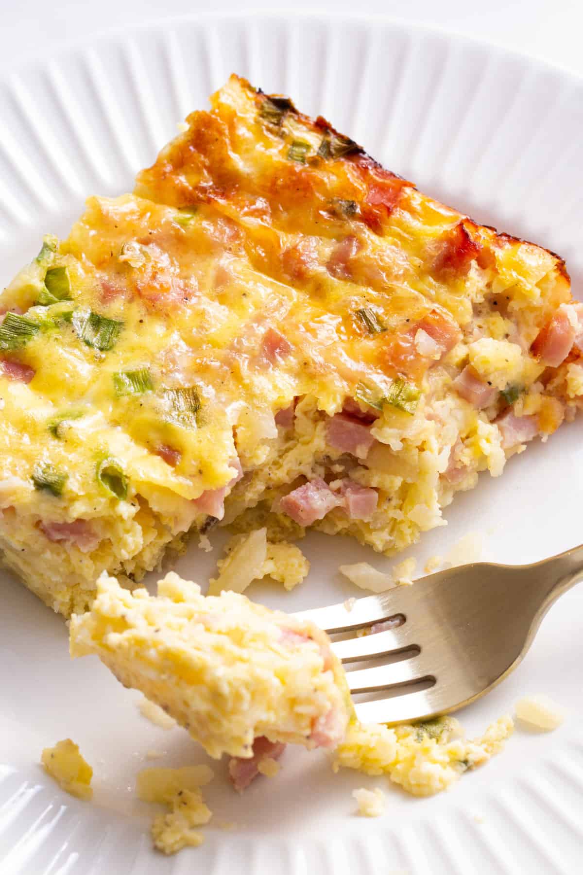 Close up image of a serving of farmer's breakfast casserole sitting on a white round plate with a forkful of casserole