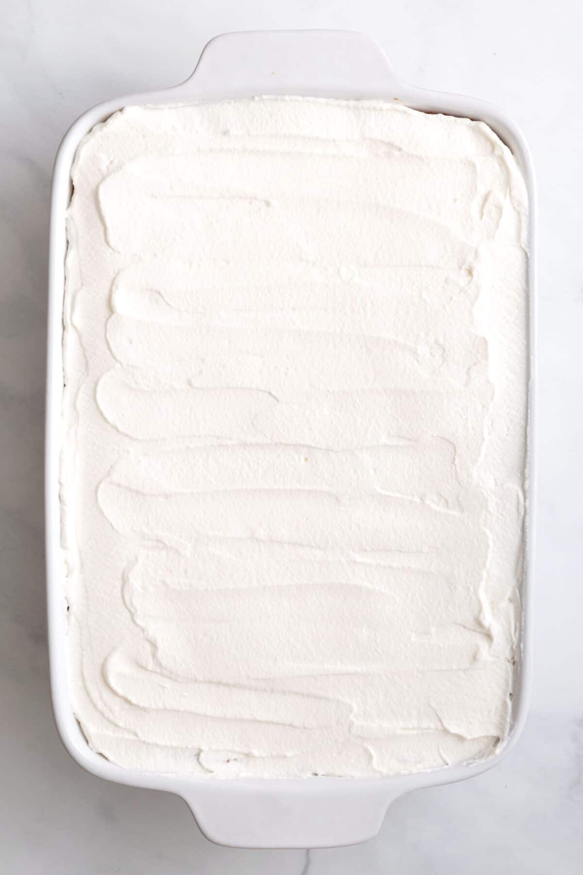 baked pineapple angel food cake topped with Cool Whip sitting in a 9x13 baking dish