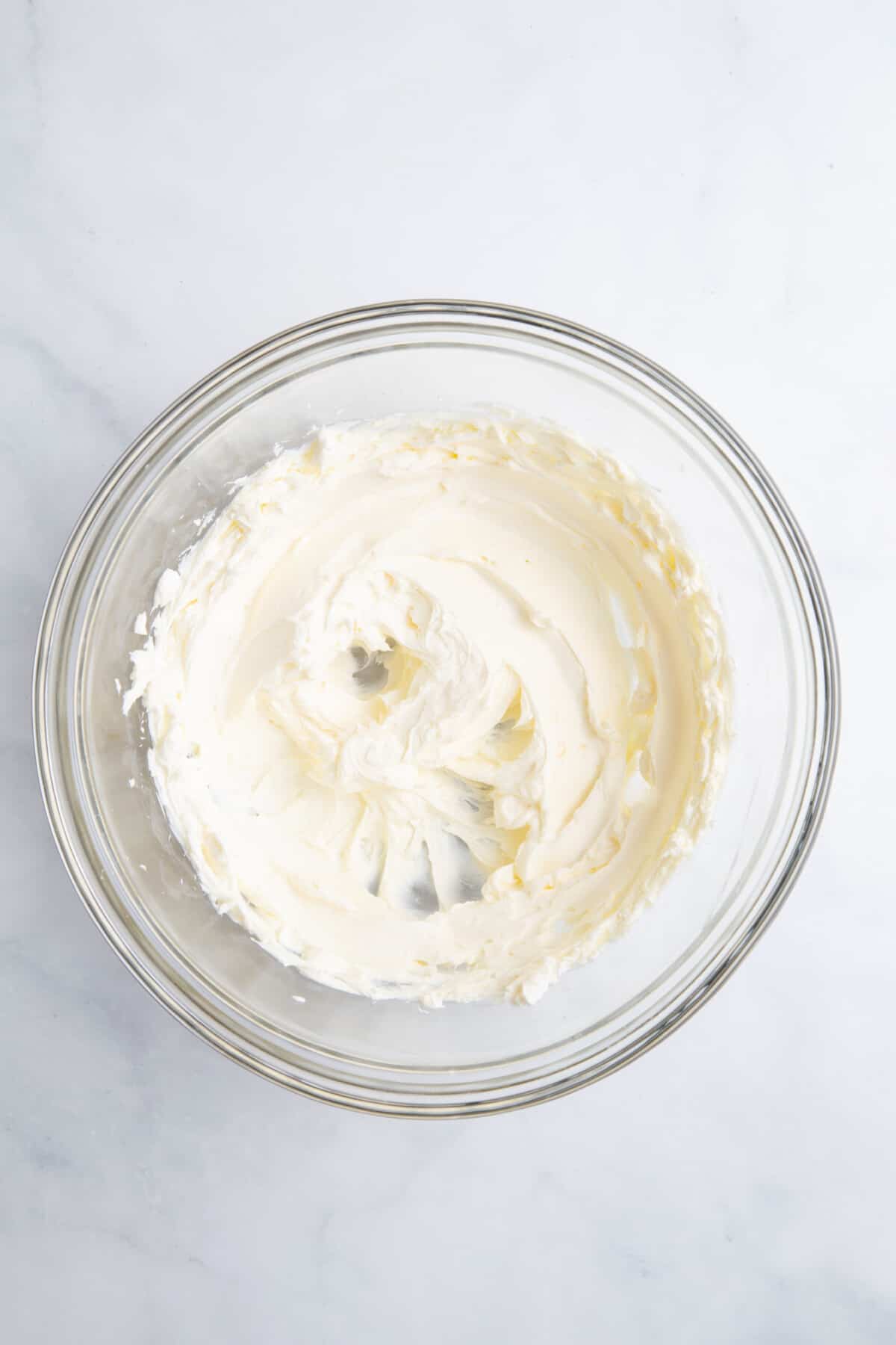 large glass bowl of cream cheese whisked until light and fluffy.