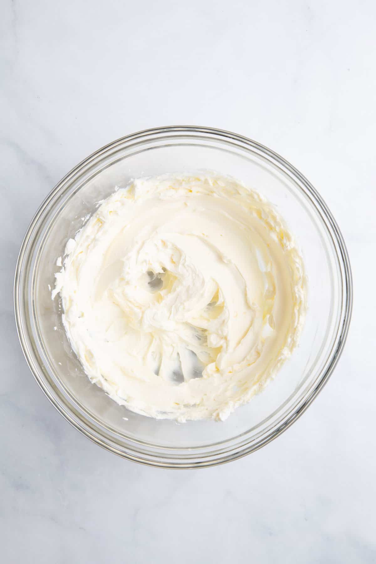 large glass bowl of cream cheese whisked until light and fluffy