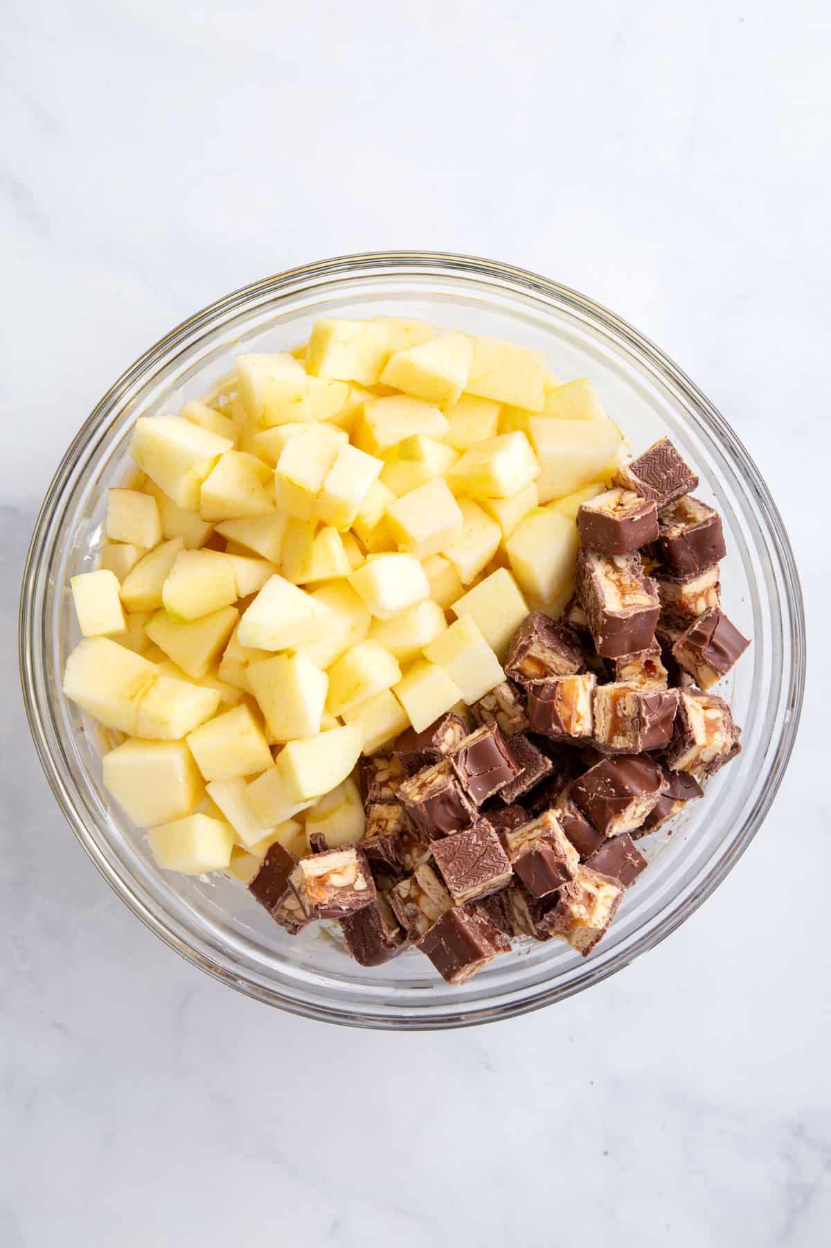 large glass bowl of chopped cubed apples and snickers bars
