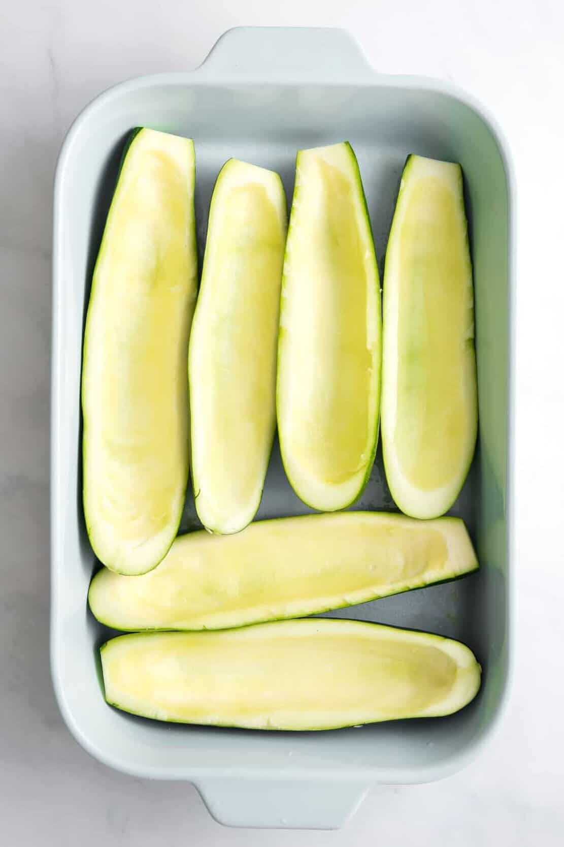 prepped zucchini with the inside flesh spooned out and lined in a blue 9x13 casserole dish