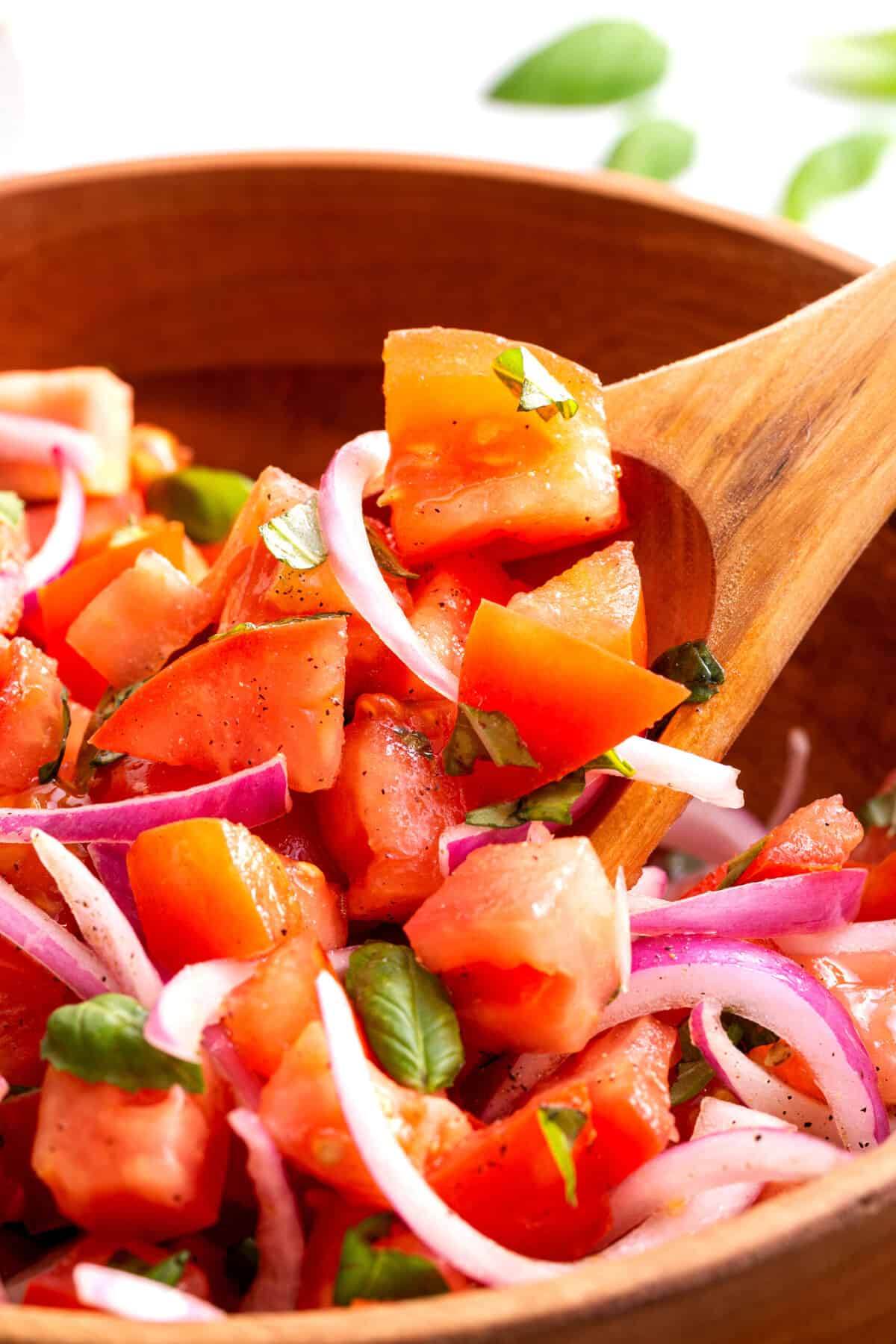 wooden bowl with tomato salad with a wooden spoon digging in