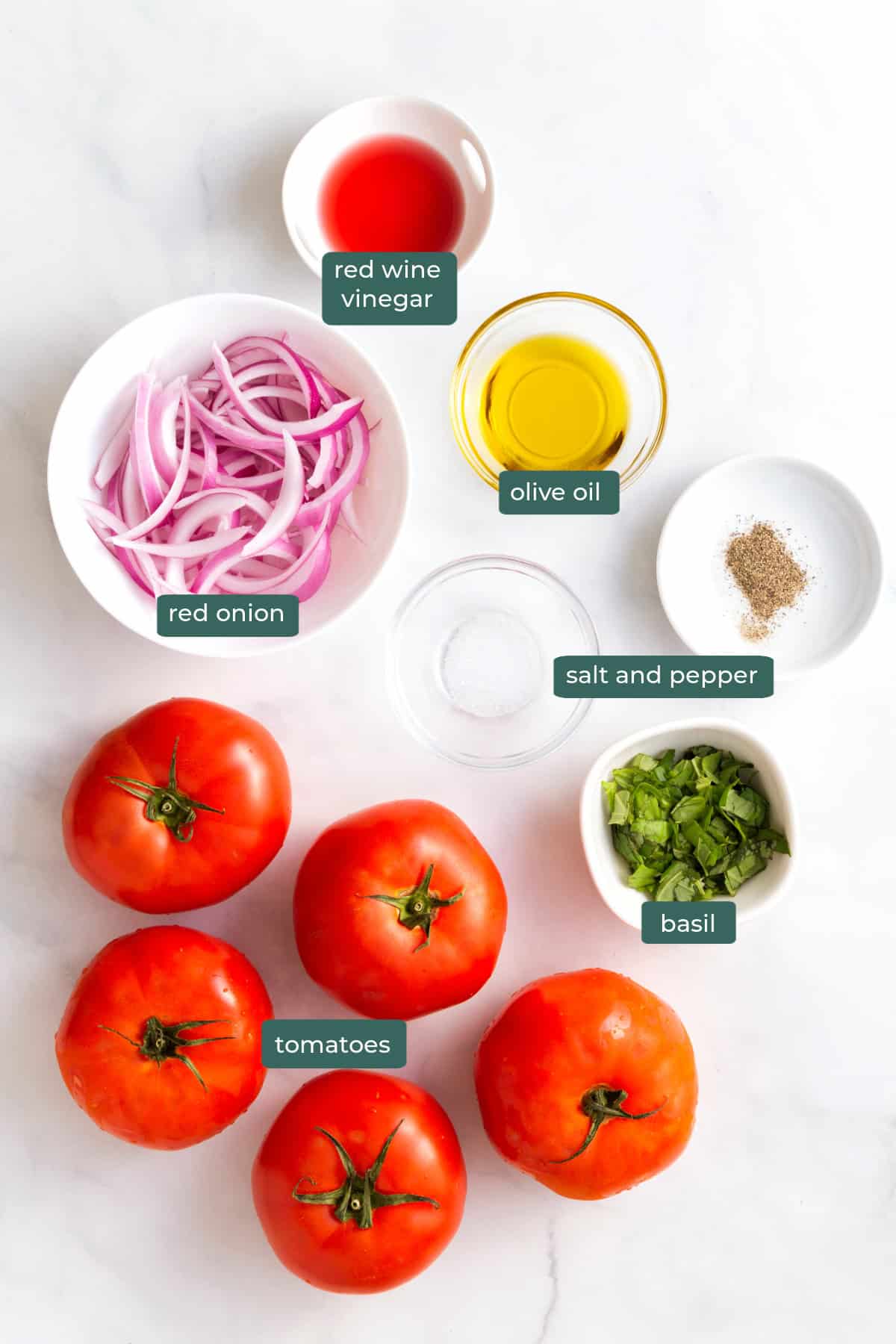 All of the ingredients for tomato salad in bowls on a countertop.
