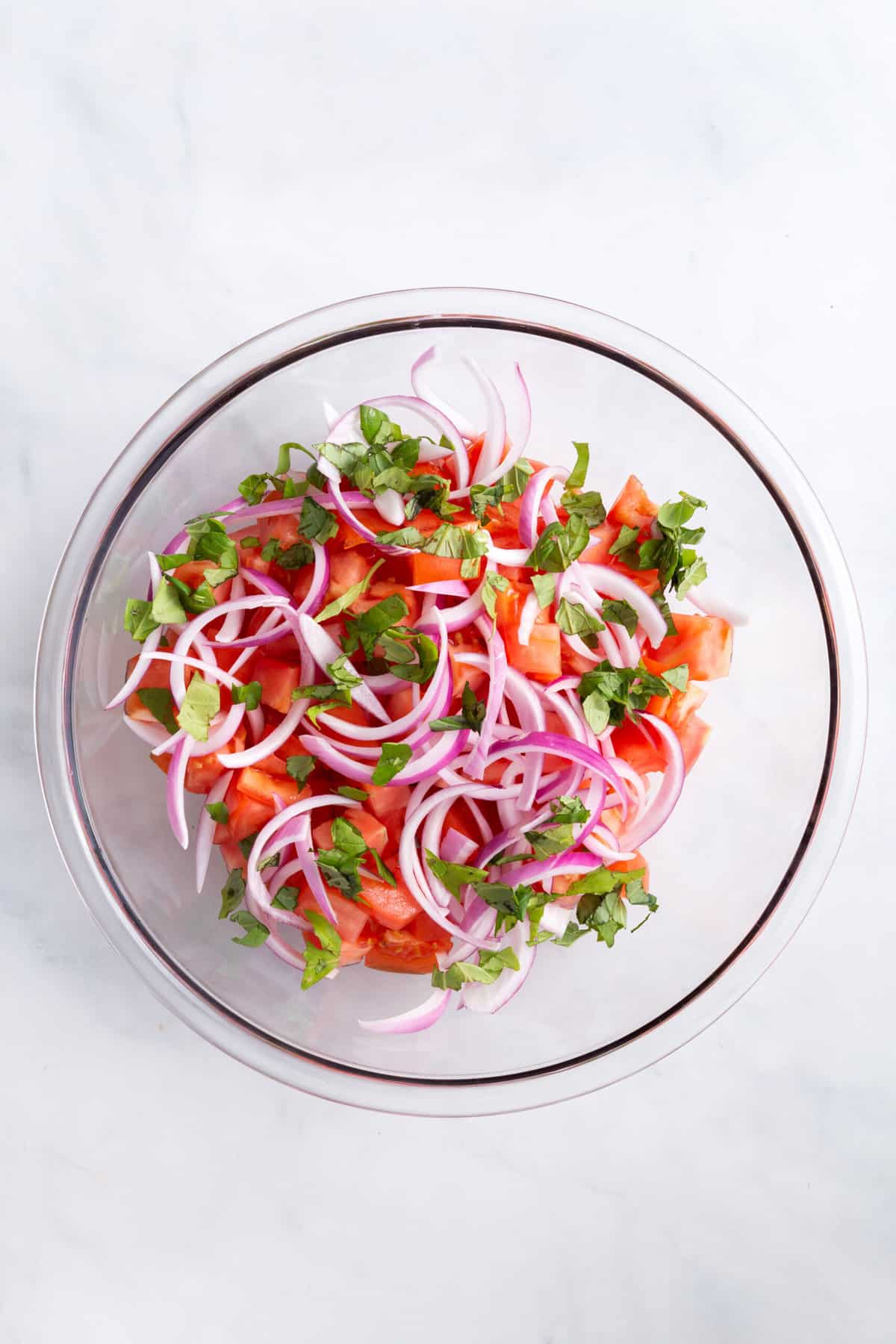 top down image of a large glass bowl with chopped tomatoes, red onion and basil