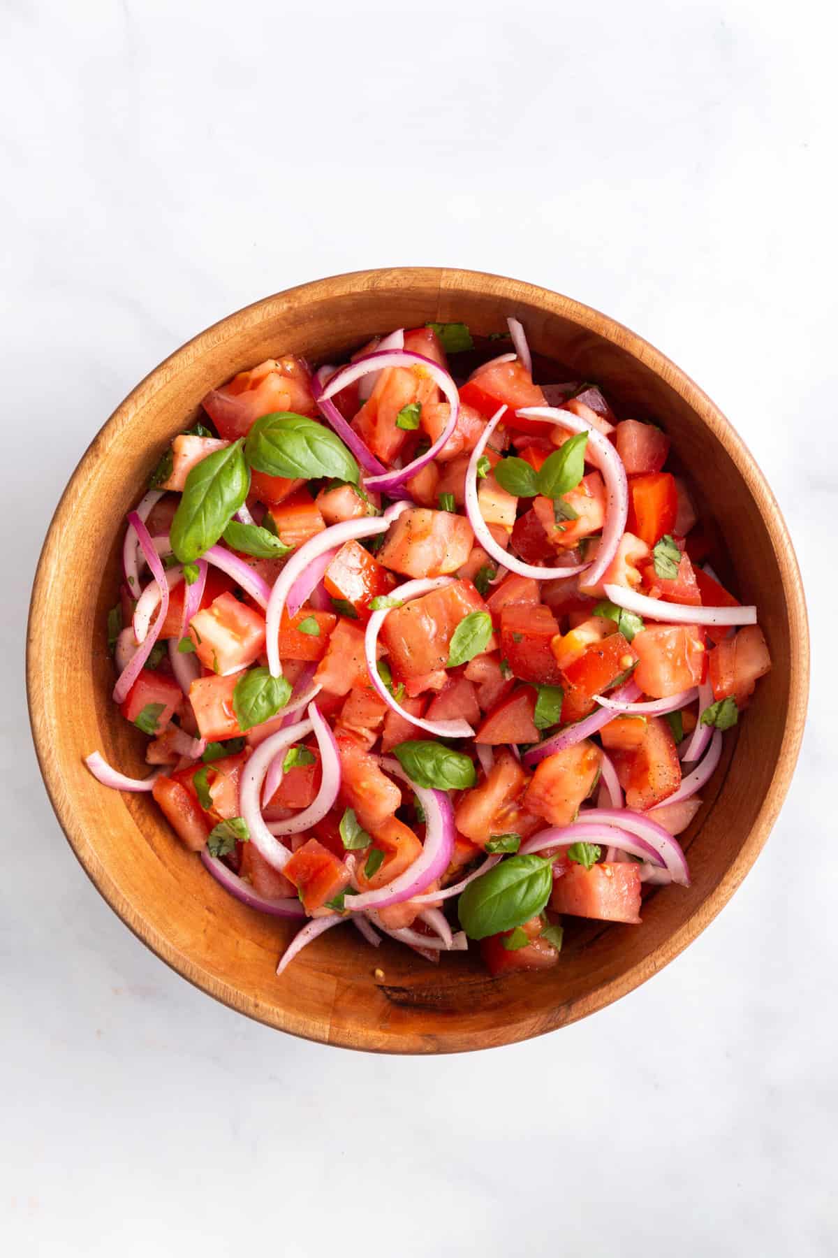 top down image of a wooden bowl with tomato salad