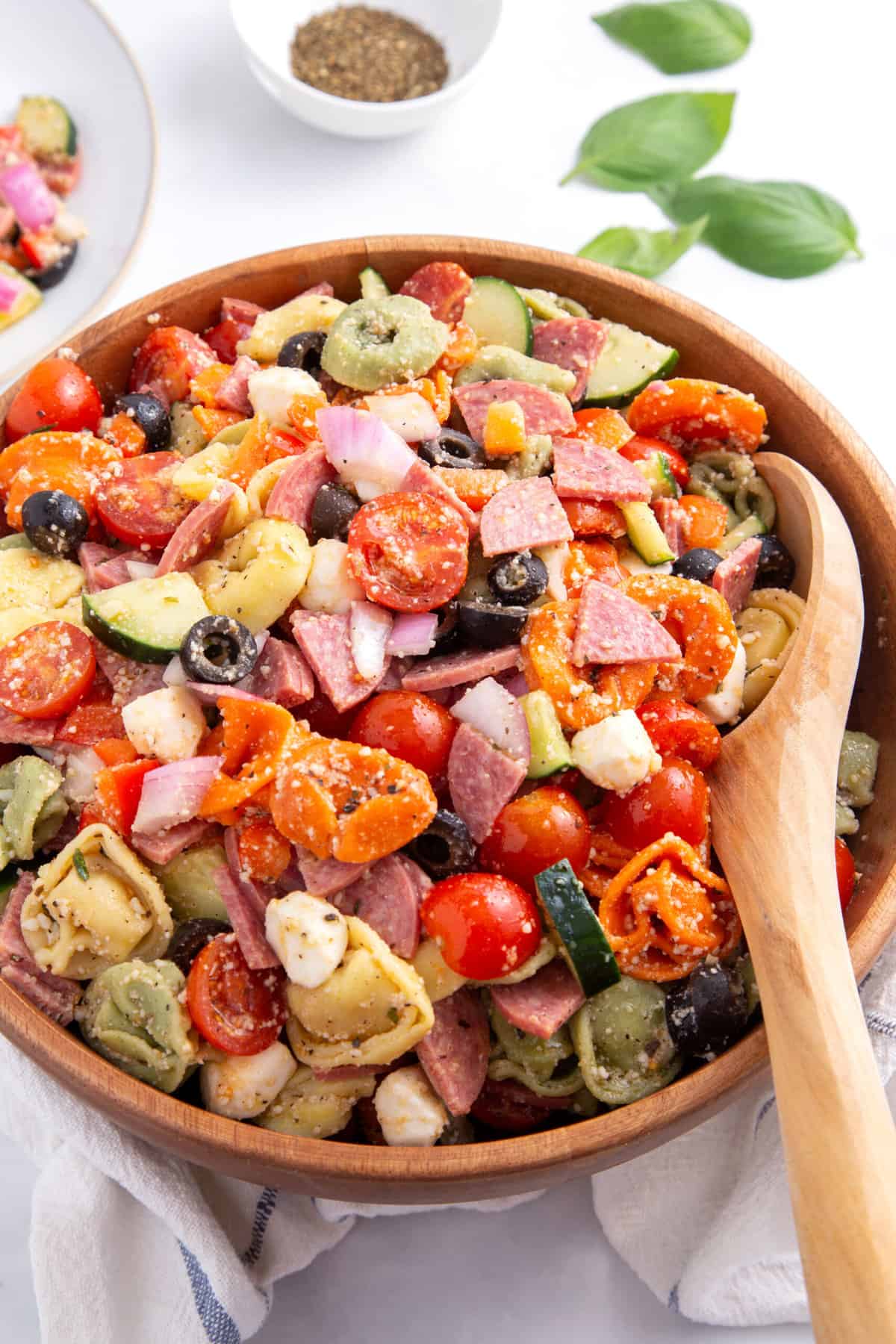top down image of a wooden bowl of tortellini pasta salad with a large wooden spoon sitting in the bowl