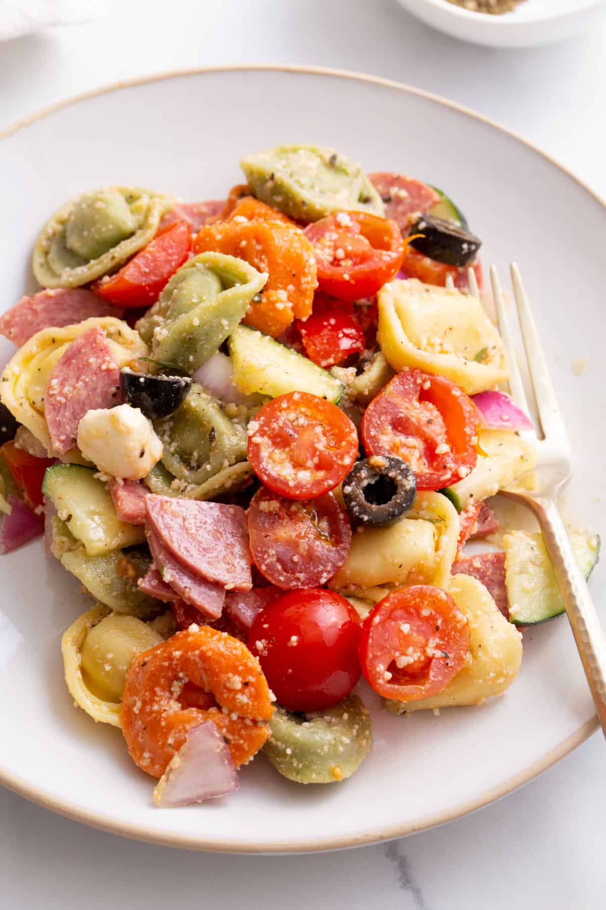 serving of tortellini pasta salad on a white round plate with a gold fork