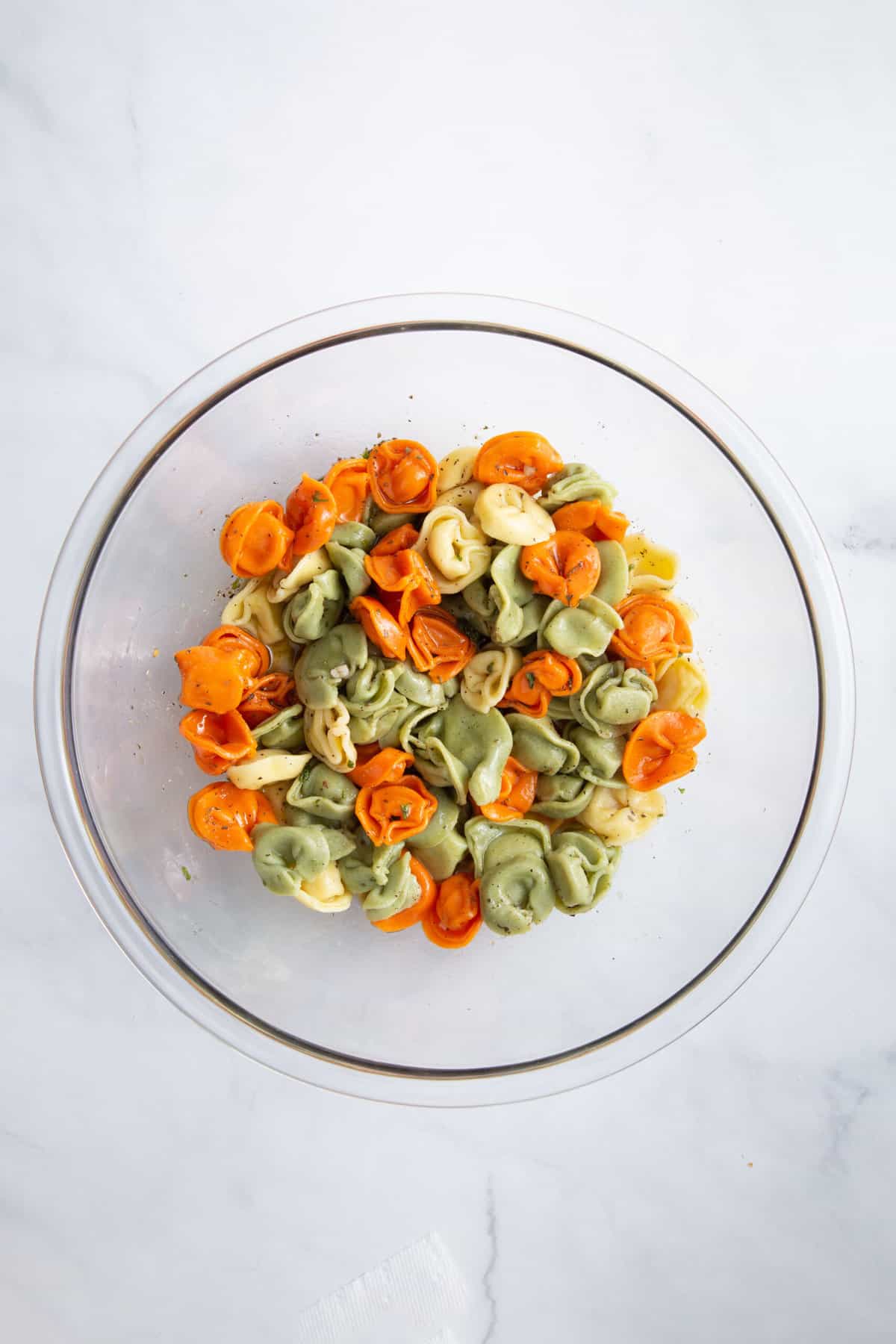 cooked tri-colored tortellini pasta tossed in italian dressing sitting in a large glass bowl