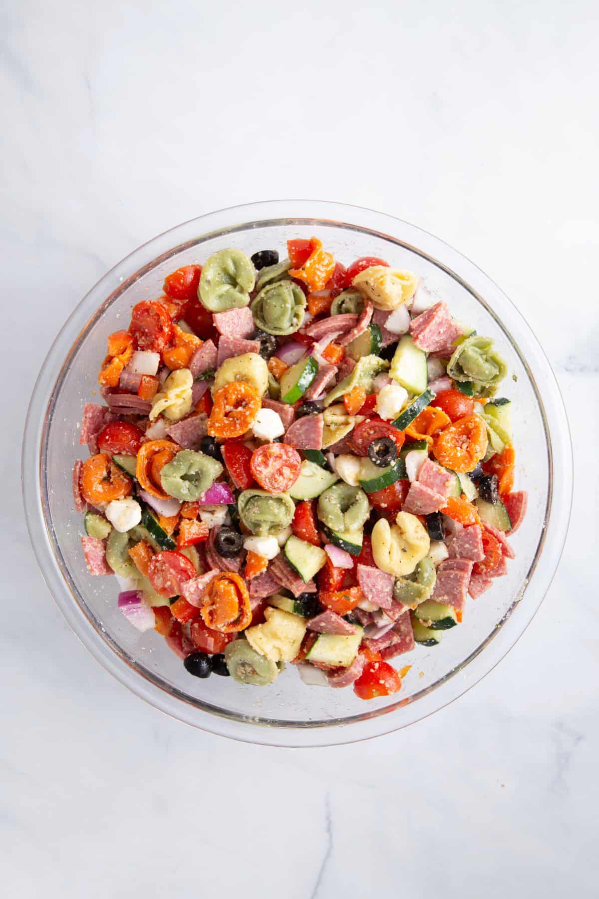 cooked tri-colored tortellini pasta tossed in italian dressing and cut vegetables and feta sitting in a large glass bowl