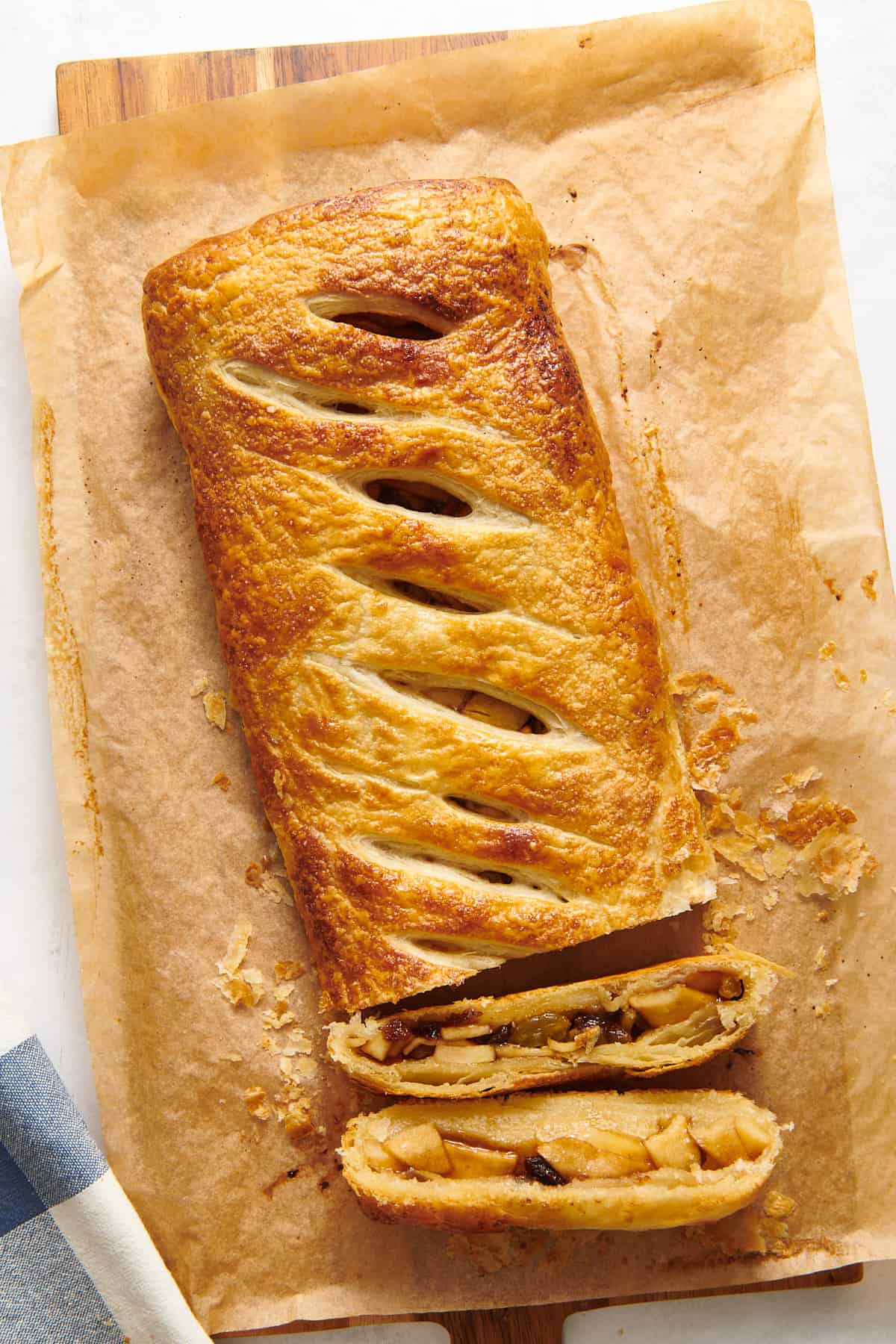 top down image of baked apple strudel sitting on parchment paper on a wood board with two slices cut showing the cross section