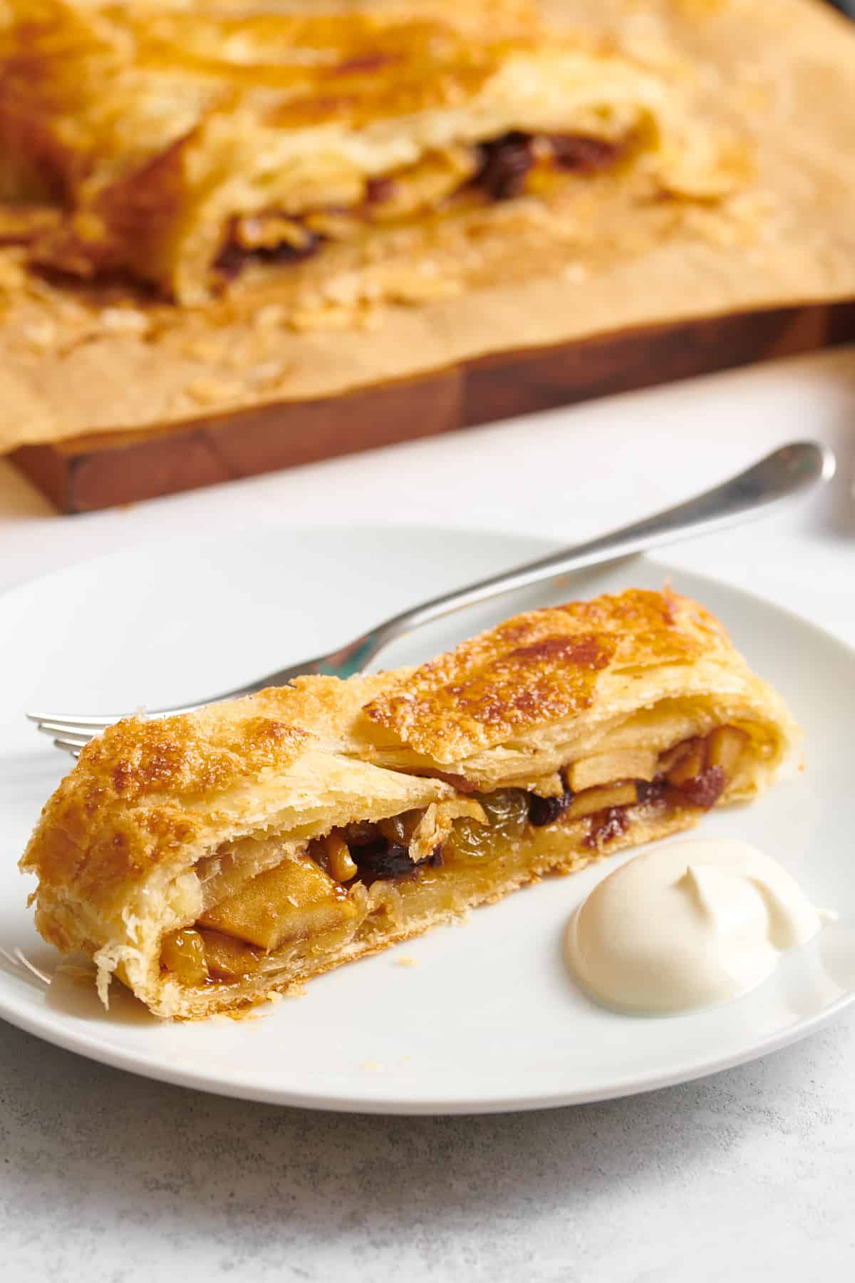 serving of apple strudel served on a white round plate with a side of whipped cream