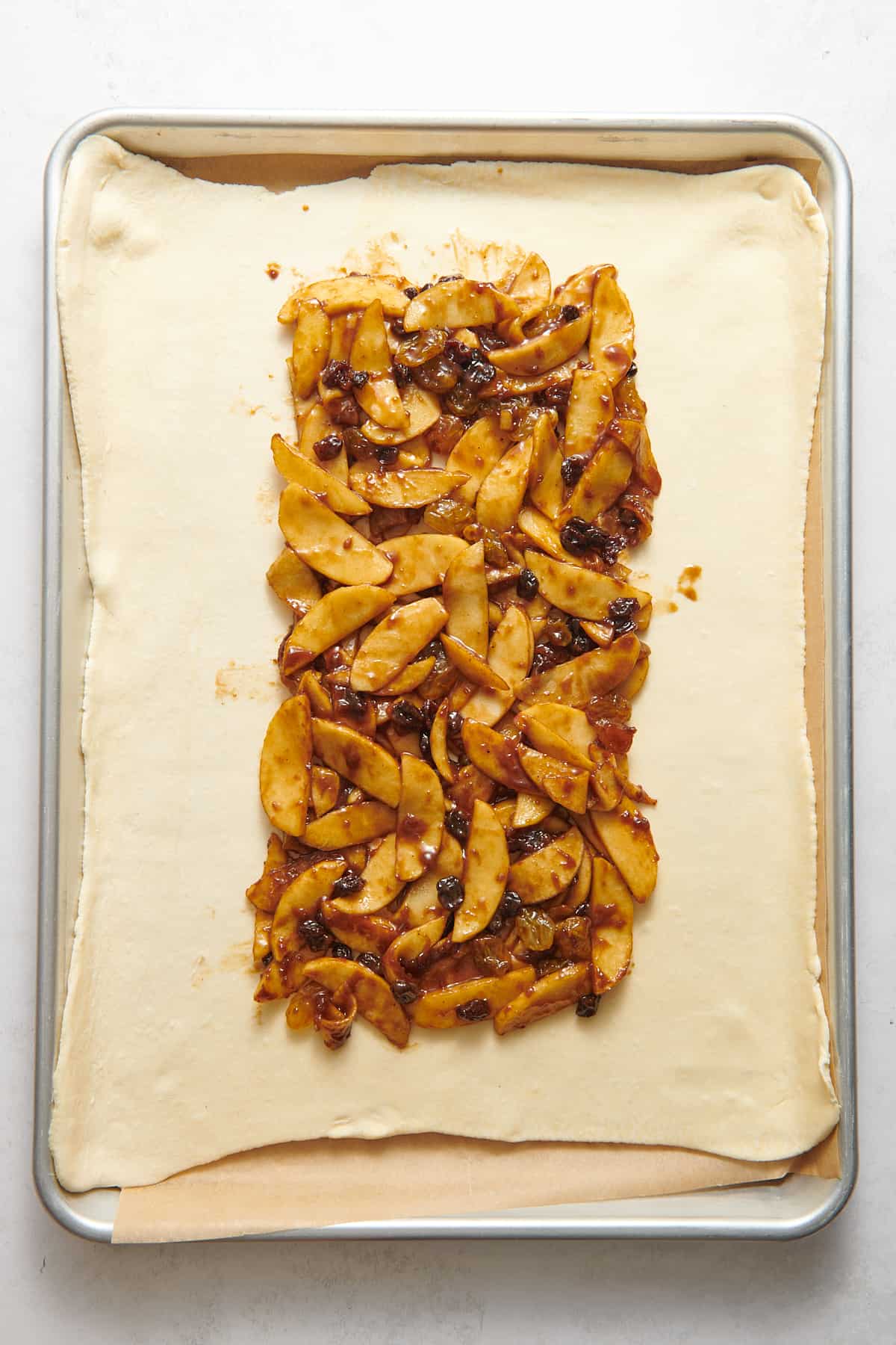 pastry dough lined on a baking tray with parchment paper layered with apple strudel filling