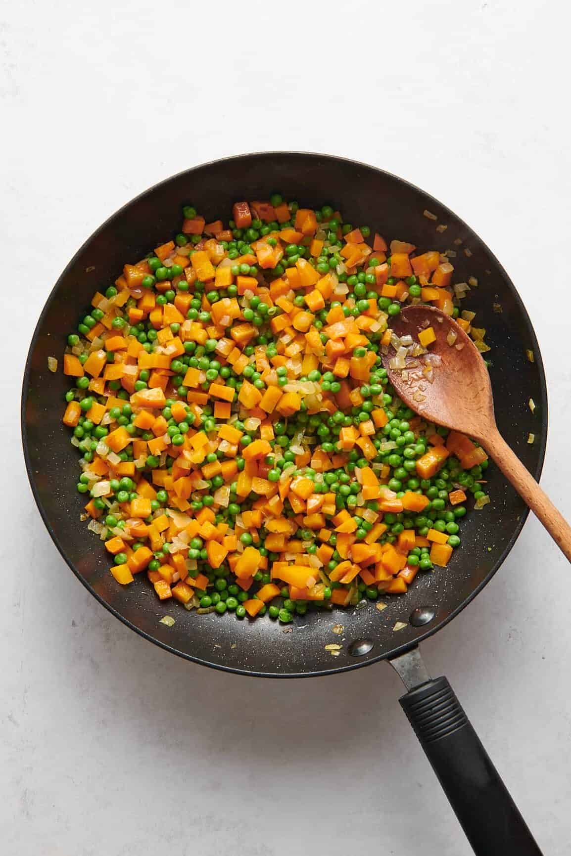 large skillet with chopped carrots and peas