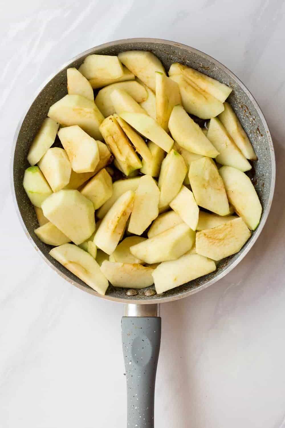 skillet with melted butter, brown sugar, cinnamon, cloves, and salt with sliced apples layered on top