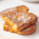 Two pieces of eggnog French toast topped with powdered sugar.