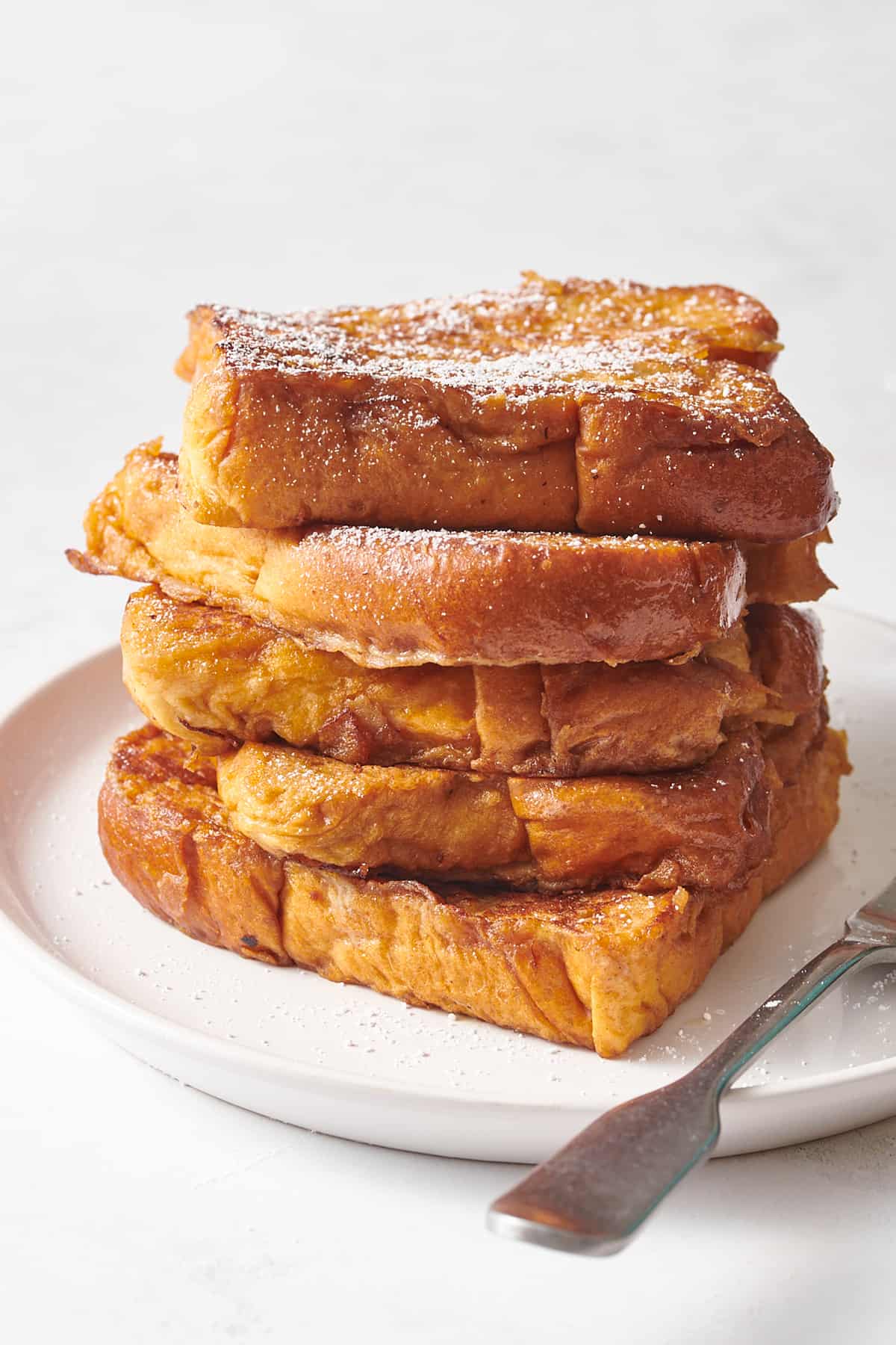 stack of five eggnog french toast served on a white round plate.