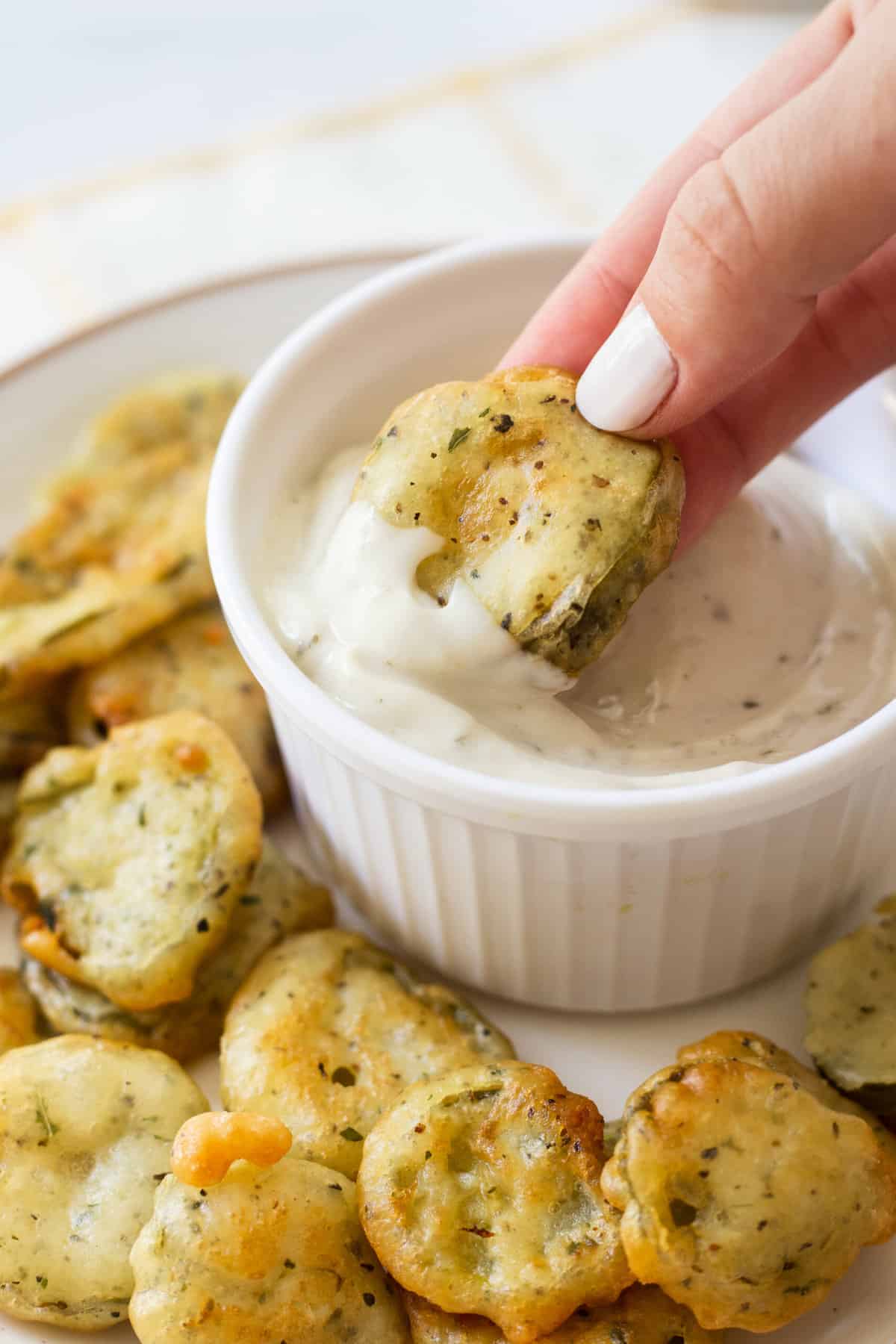 hand taking a fried pickle and dipping it into a ceramic bowl with ranch dressing