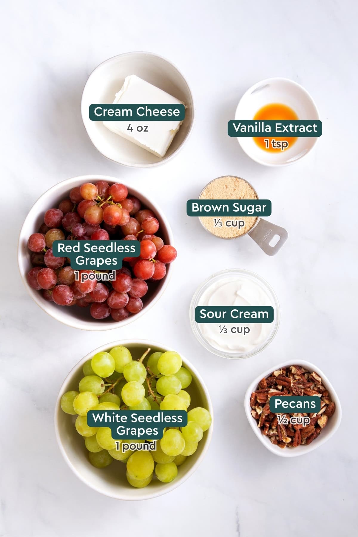 All of the ingredients for grape salad in bowls on a white countertop.