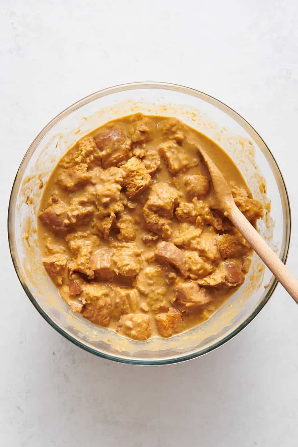 pumpkin bread pudding mixture sitting in a large glass bowl with a wooden spoon