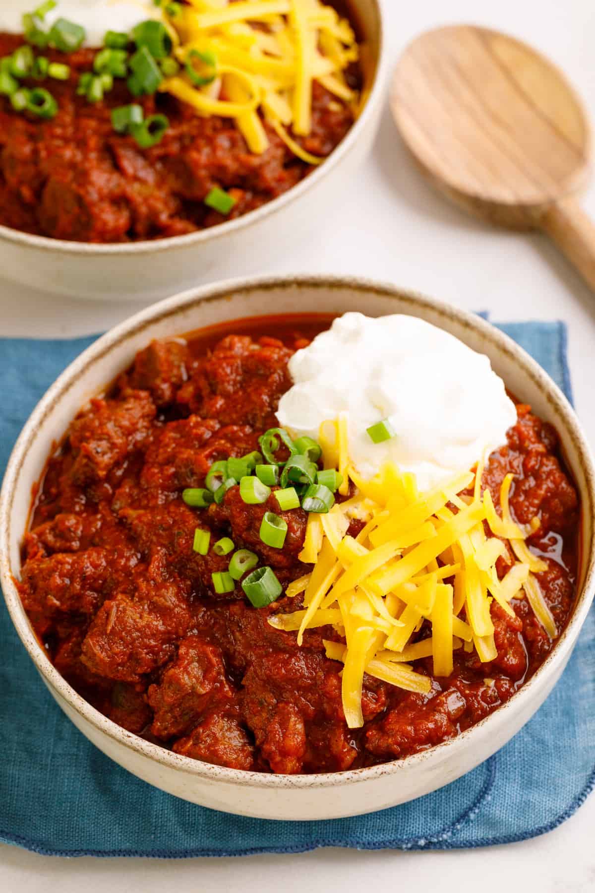 bowl of texas chili topped with chopped green onions, sour cream and shredded cheddar cheese