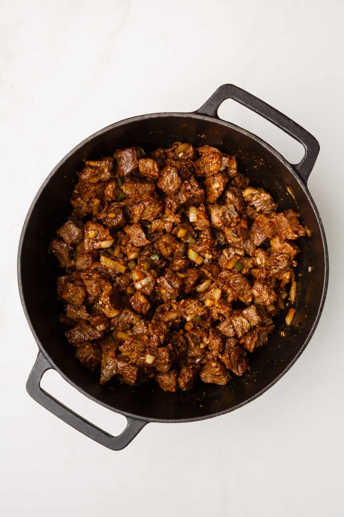 dutch oven with cooked beef cubes, sauteed onion, garlic and jalapenos