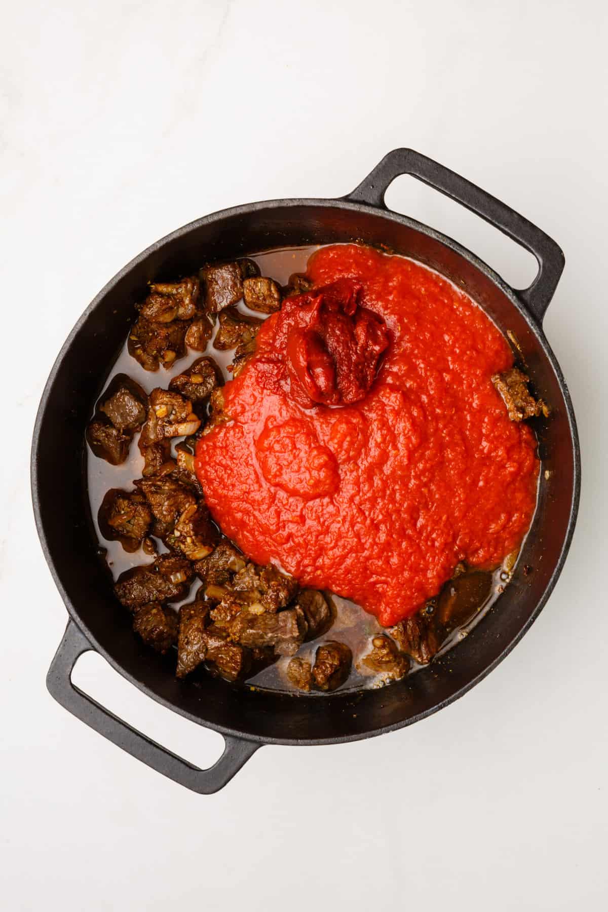 dutch oven with cooked beef cubes, sauteed onion, garlic and jalapenos with tomato paste and broth