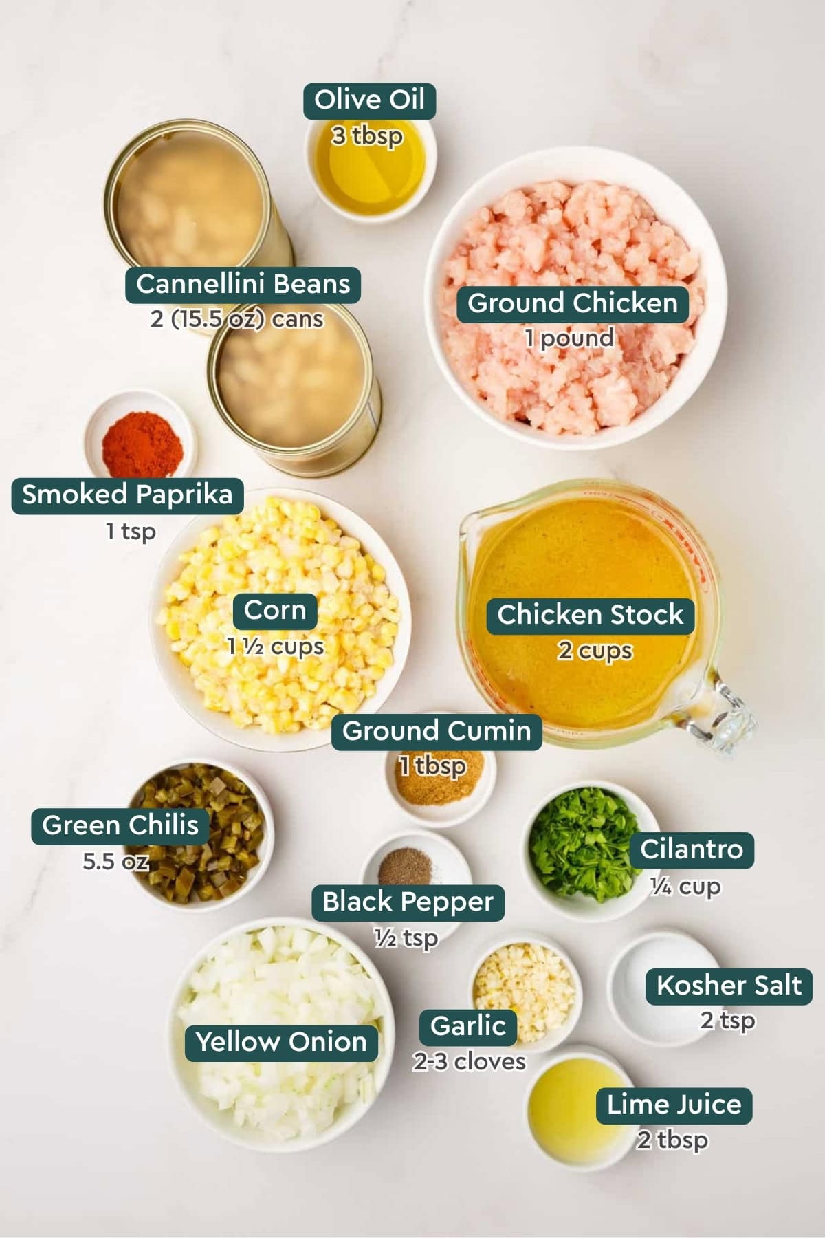 All of the ingredients for creamy white bean chicken chili in bowls on a white countertop.