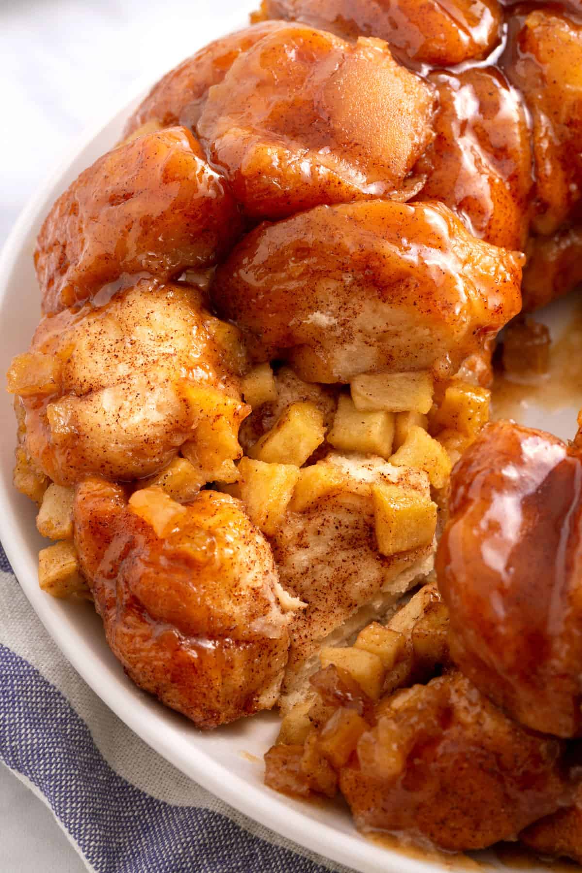 close up image of caramel apple monkey bread served on a white round plate and showing the cross section