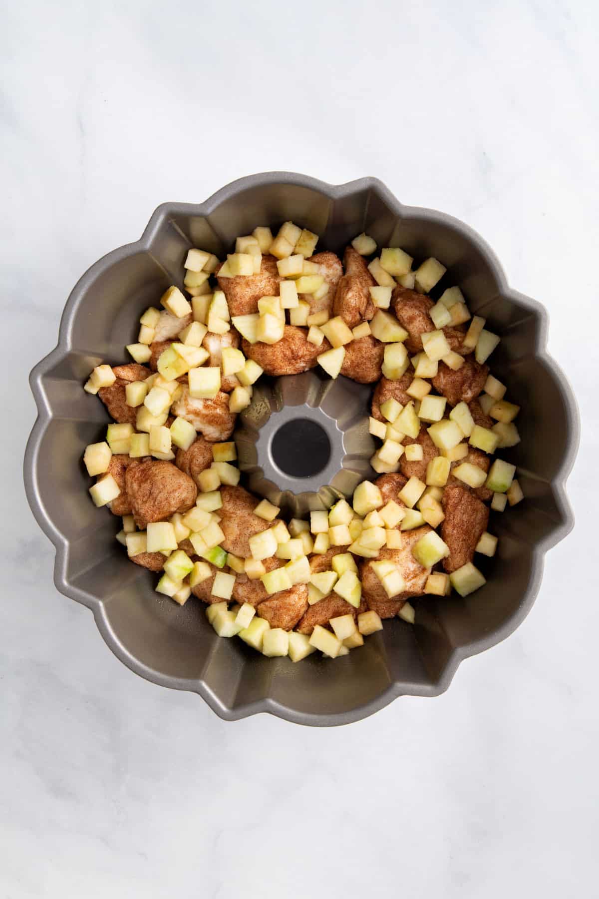 cinnamon dough pieces and chopped granny smith apples lining the bottom of a bundt cake tin