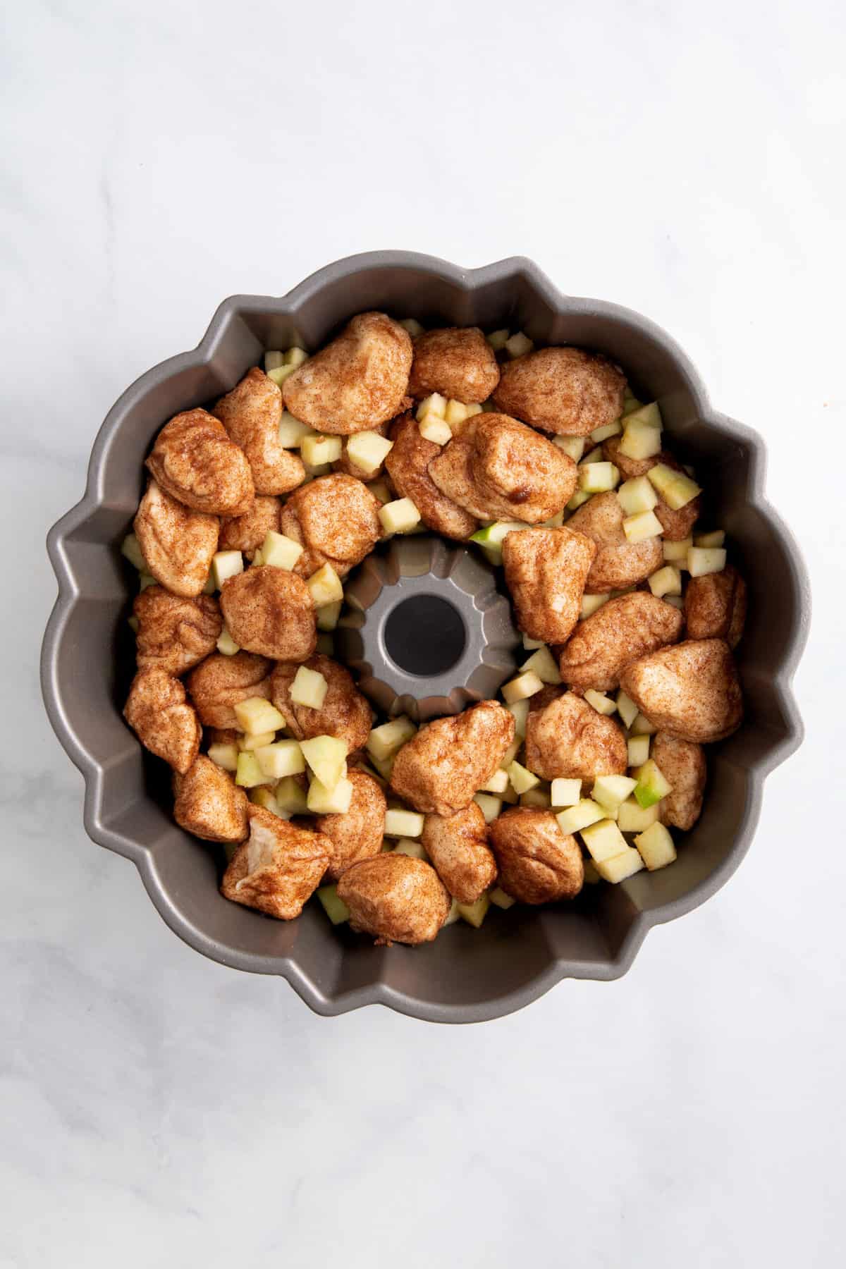 cinnamon dough pieces and chopped granny smith apples topped with more cinnamon dough sitting in a bundt cake tin