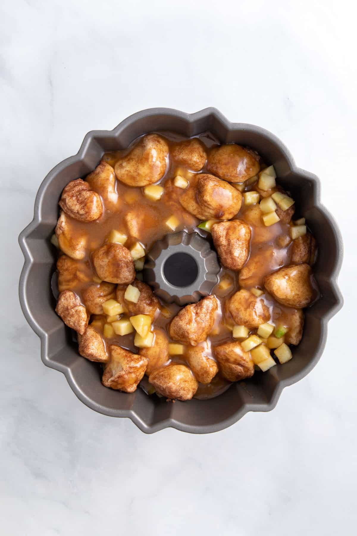 cinnamon dough pieces and chopped granny smith apples topped with more cinnamon dough and caramel sauce sitting in a bundt cake tin