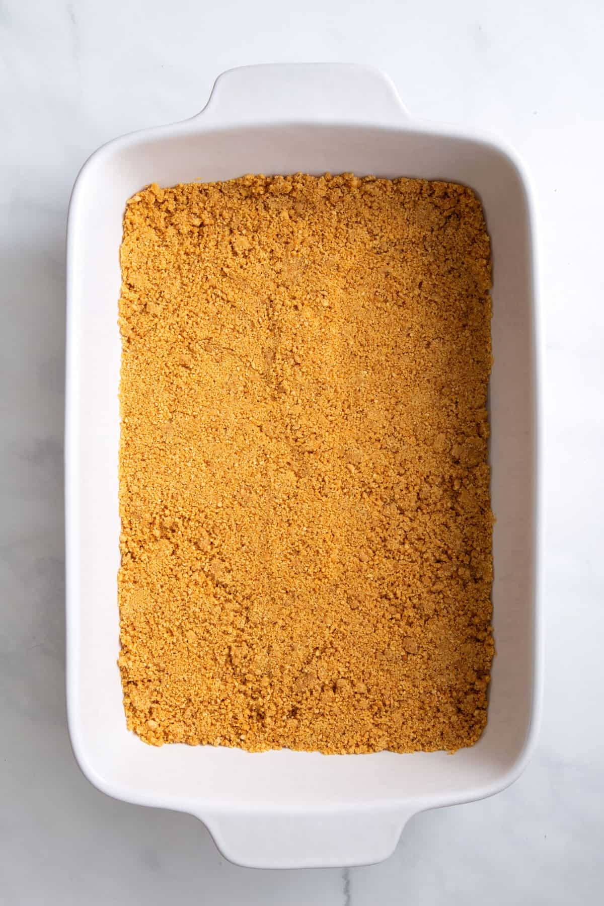 graham cracker crumb and melted butter mixture layered at the bottom of a 9x13 baking dish