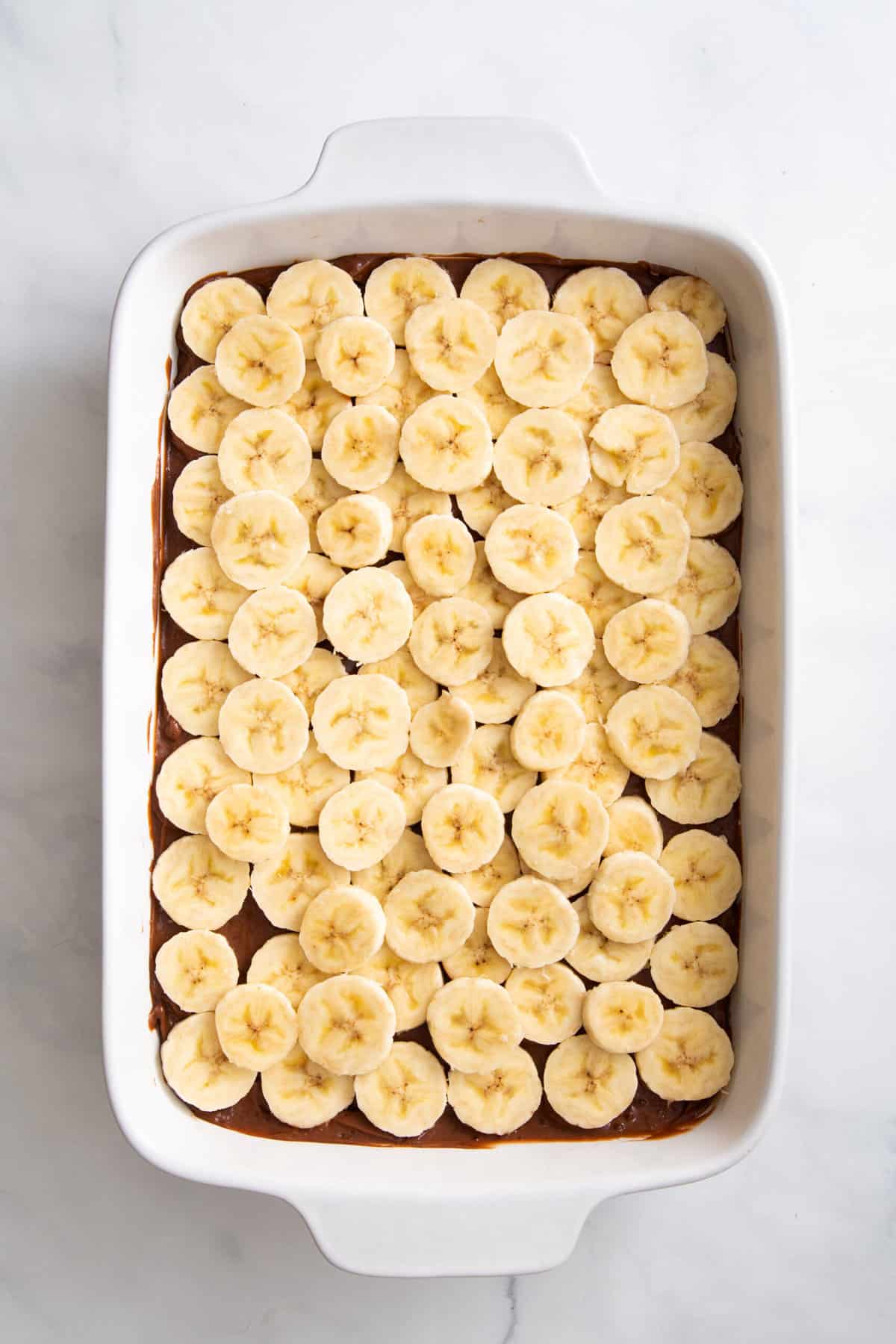 slice bananas layered on top of chocolate pudding mix in a 9x13 baking dish