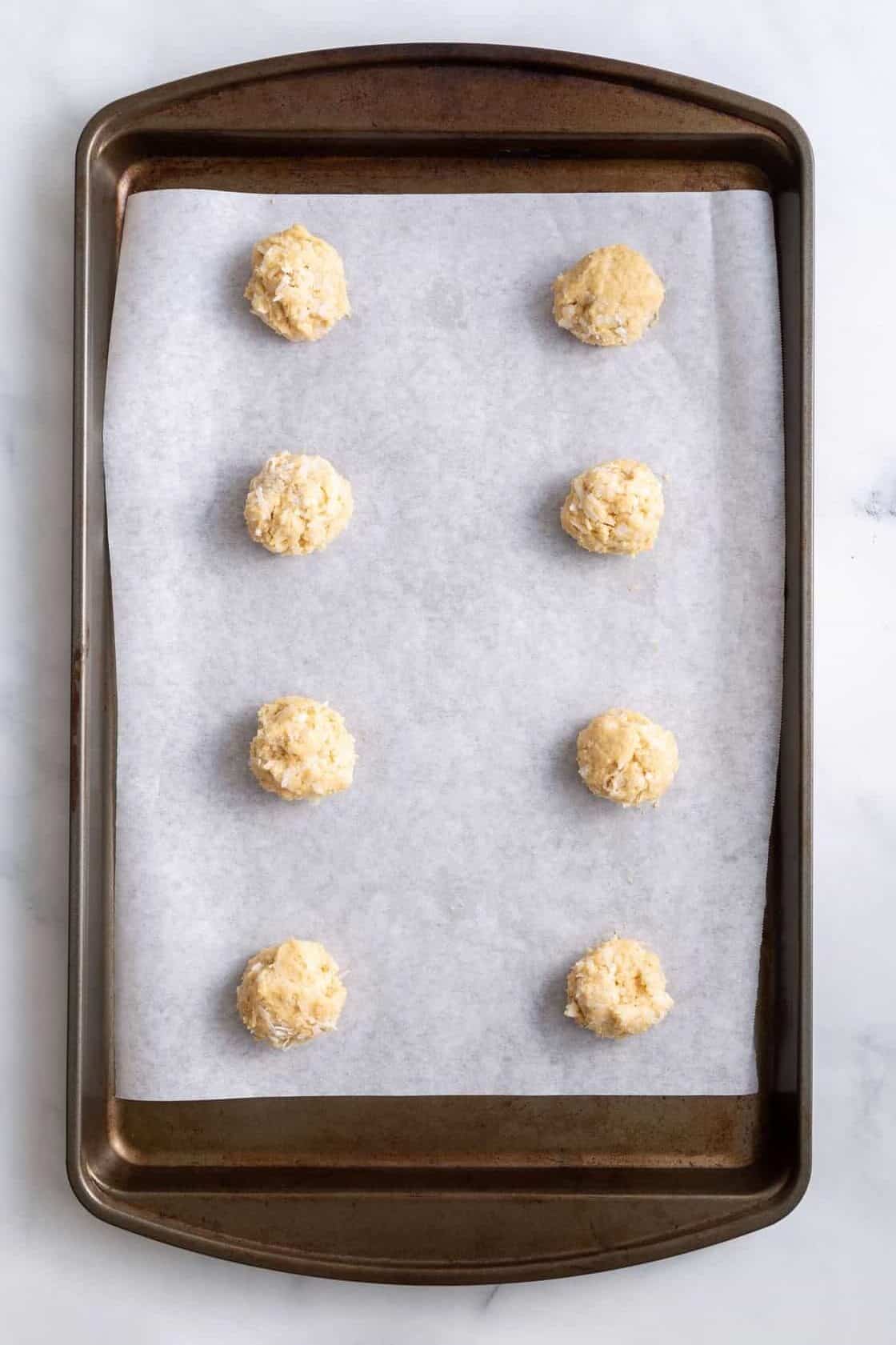 eight coconut cookie batter dough balls sitting on a baking tray with a baking sheet 