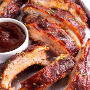 Crock pot ribs on a plate with a small bowl of BBQ sauce.